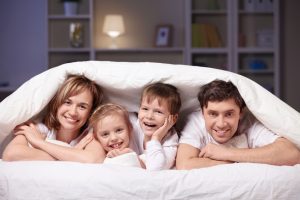 A smiling family of four laying together under a blanket.